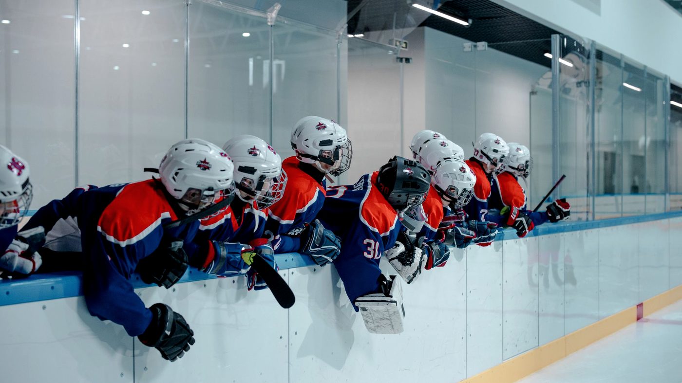 Youth hockey players leaning over the boards watching their teammates