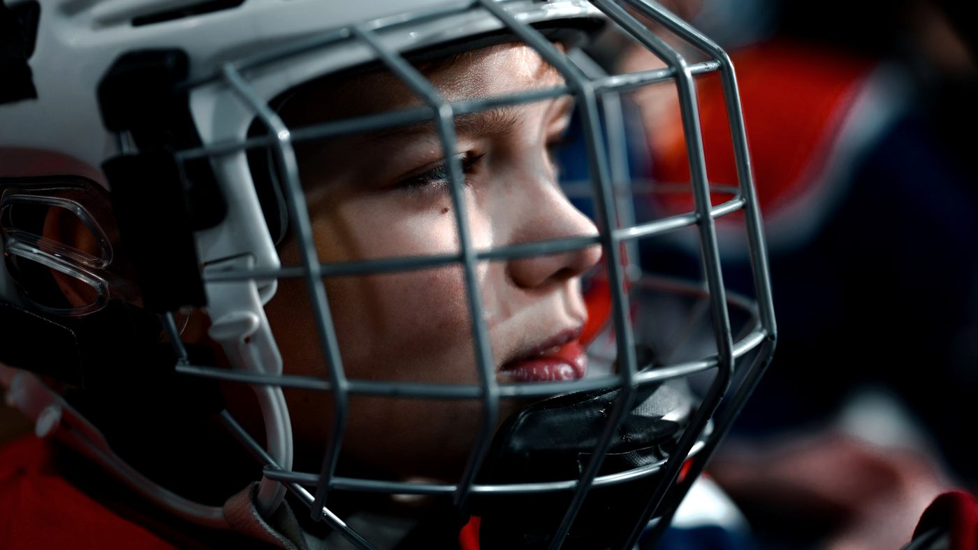 Young hockey player in a caged helmet looking up the ice