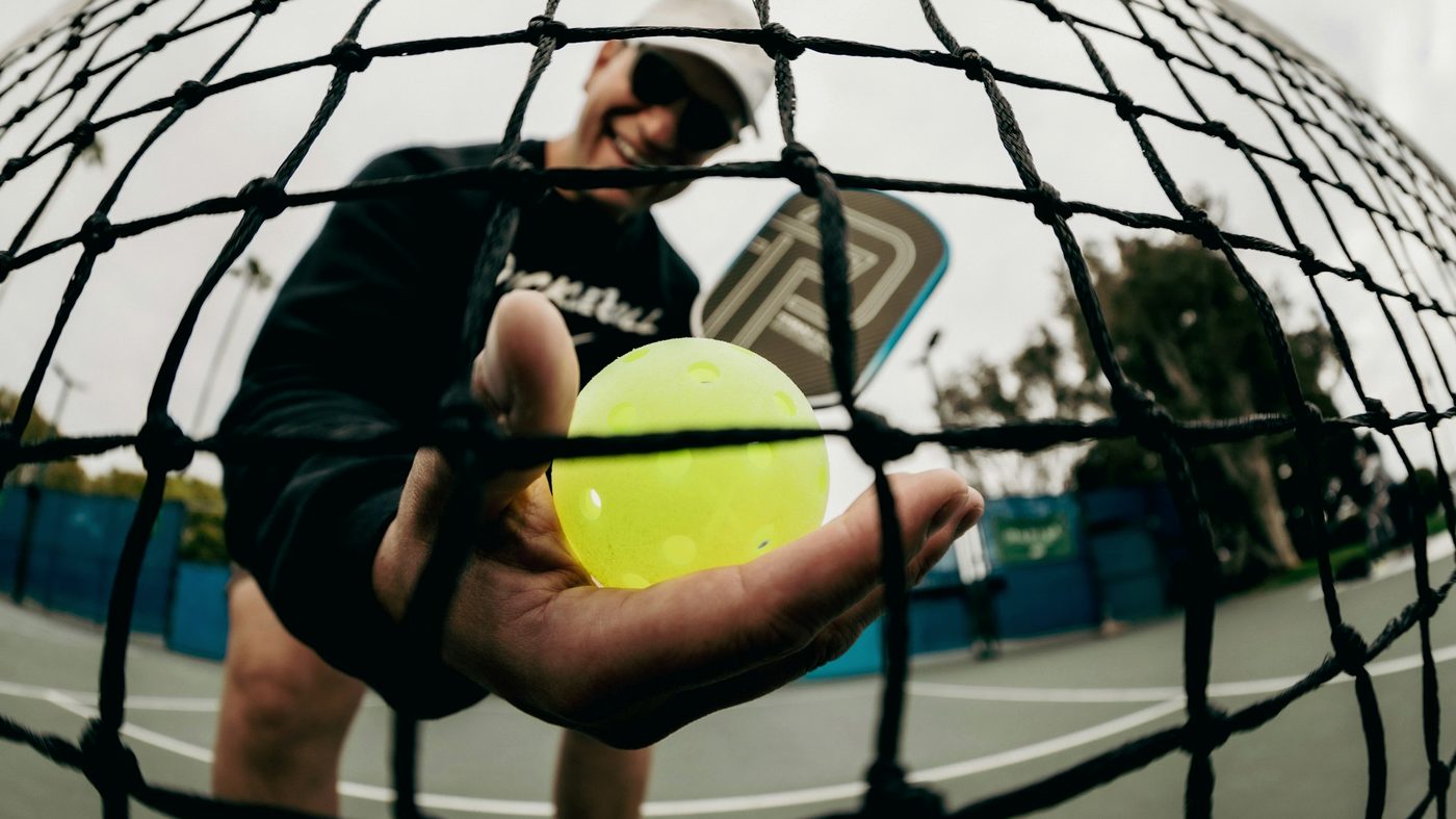 Pickleball player holding a ball up to the net
