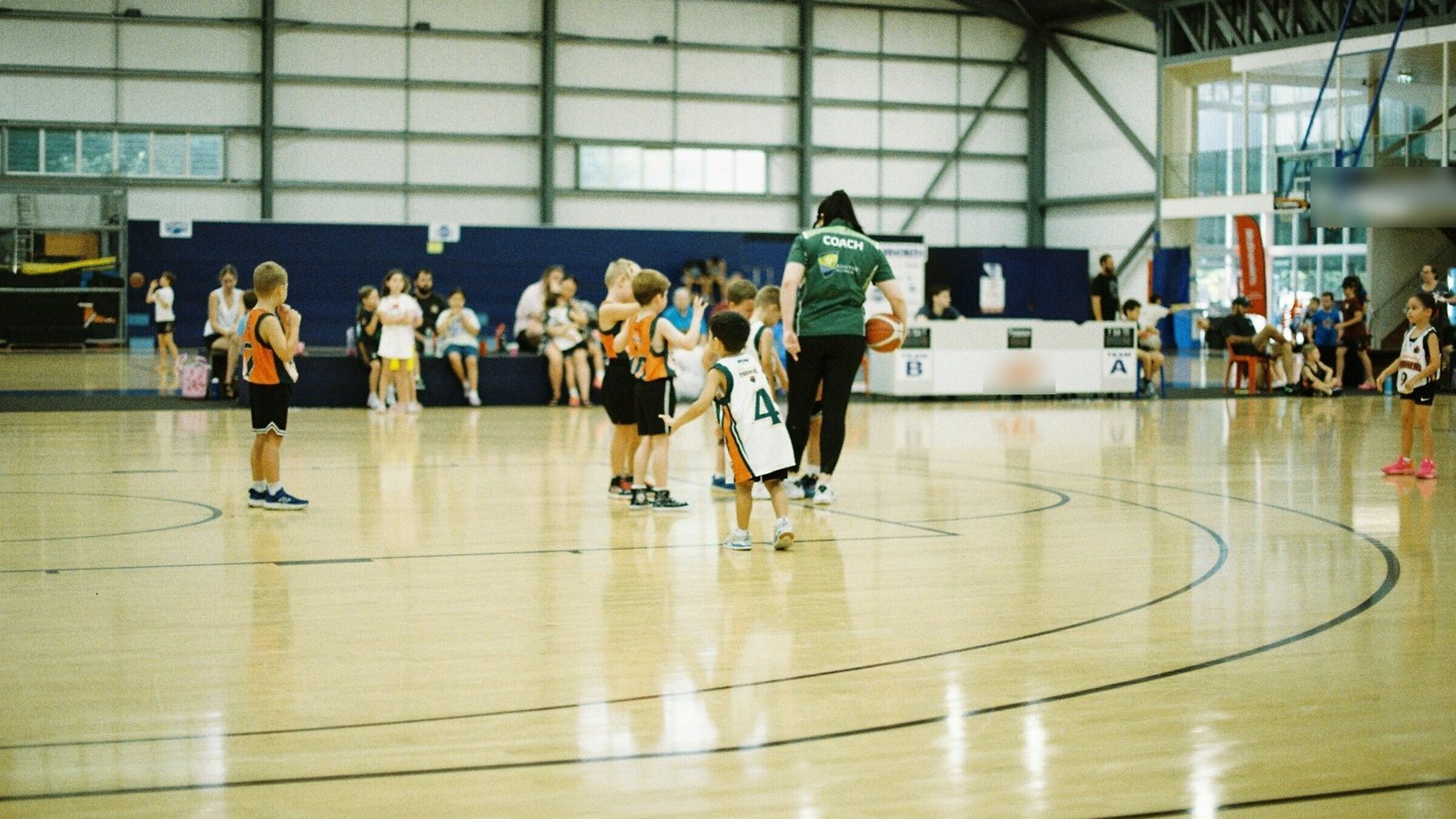 Young kids at a basketball session in a big gym with their coach