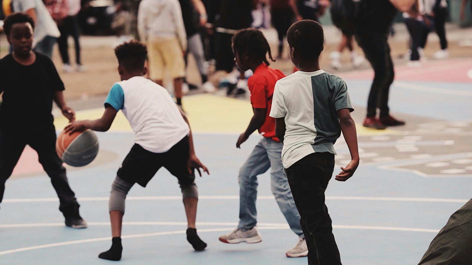 Kids playing pickup basketball on an outdoor court, one dribbling past defenders