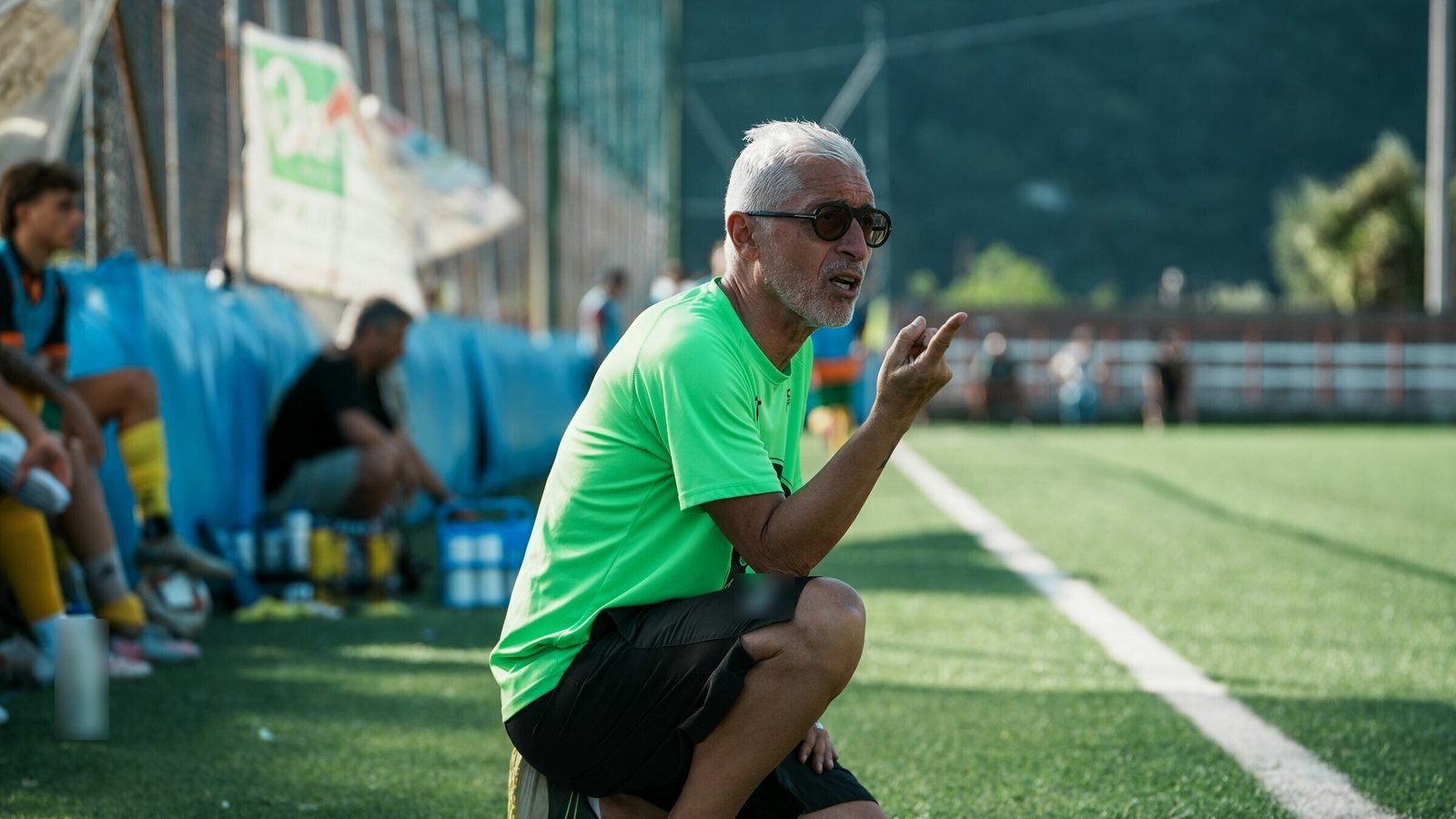 Grey-haired soccer coach crouching on the sideline, giving instructions