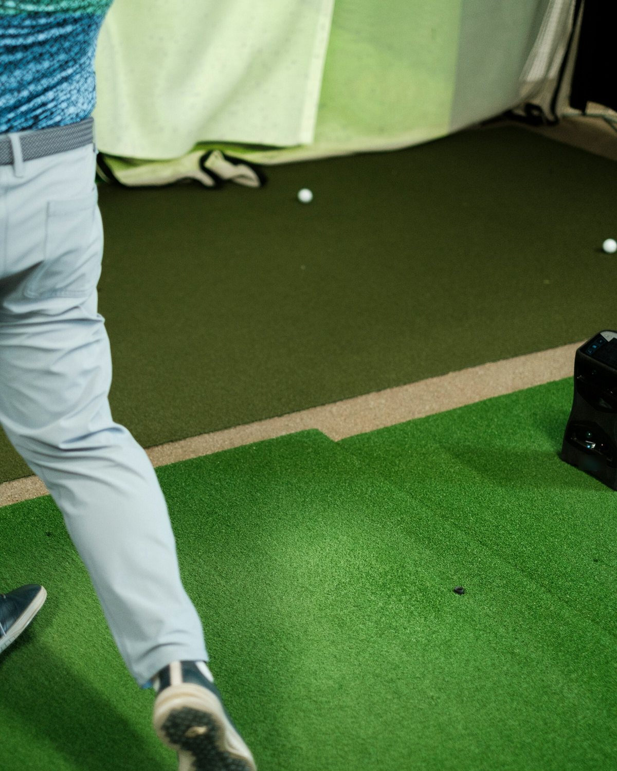 Golfer mid-swing in an indoor simulator bay, with the impact screen and launch monitor