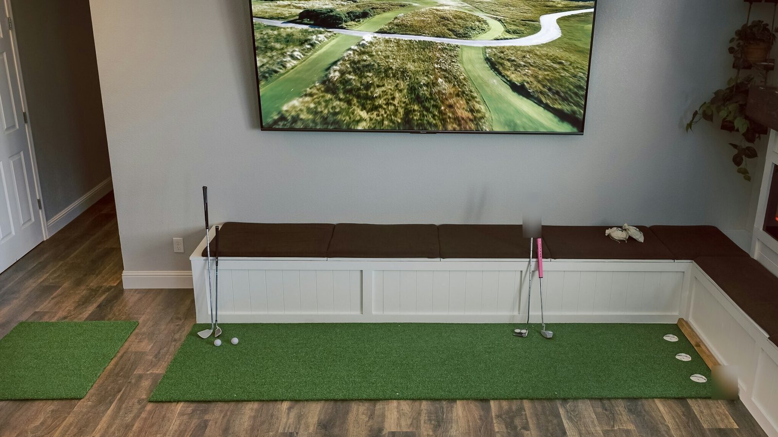 Empty indoor golf practice room with a putting mat and a golf course on screen