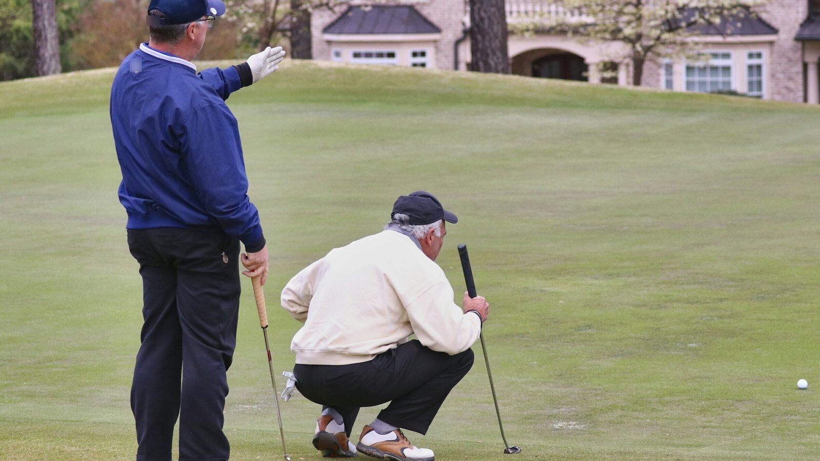 Two older golfers reading a putt together on a green