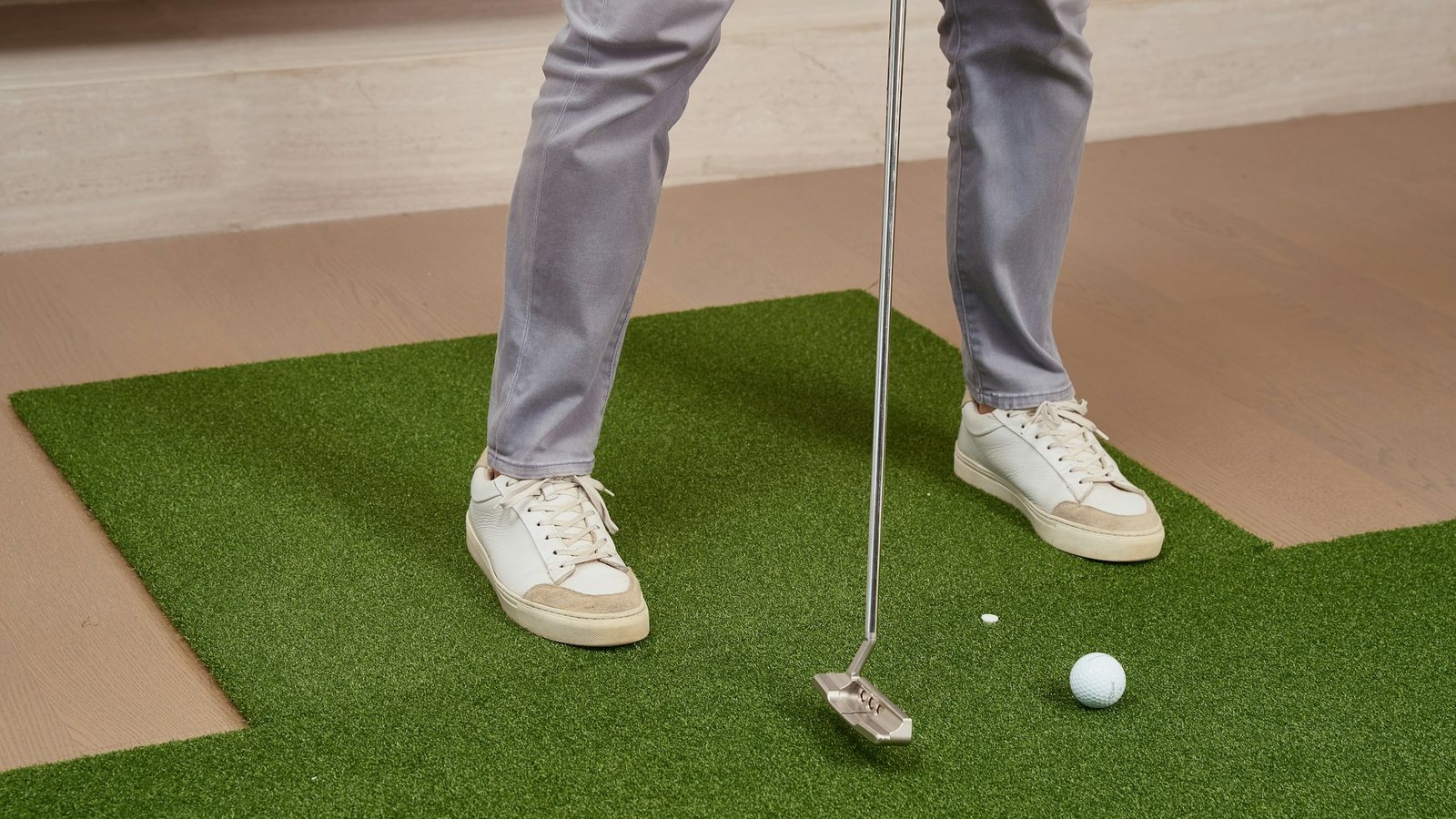 Close view of a golfer's feet and putter over a ball on an indoor mat