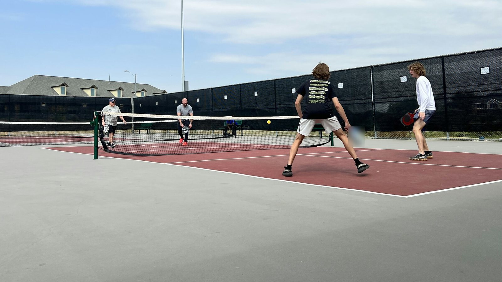 Mixed-age doubles pickleball game on an outdoor court
