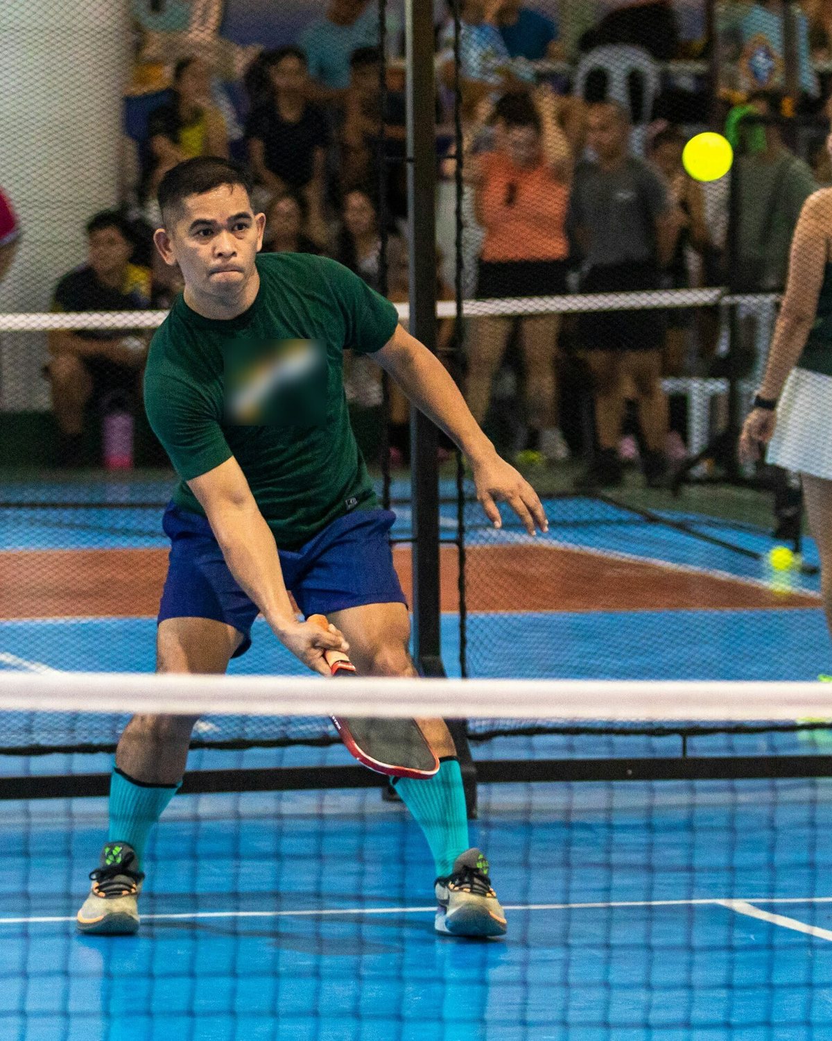 Man hitting a low volley in mixed doubles on an indoor pickleball court