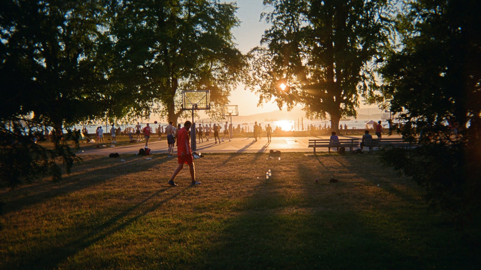 Sunset over the Kitsilano Beach basketball courts, with players and the water behind