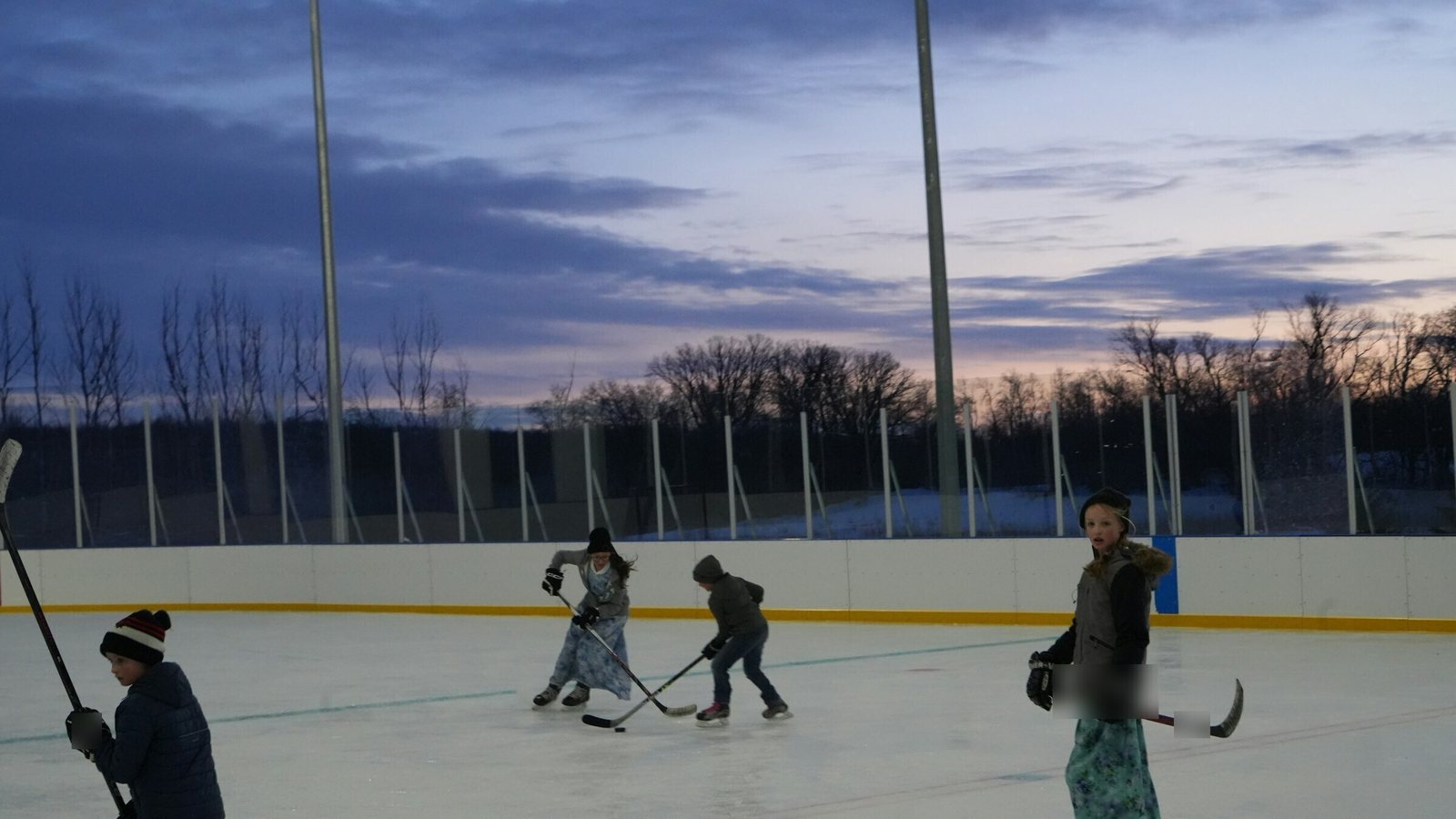 Kids playing shinny hockey on an outdoor community rink at dusk